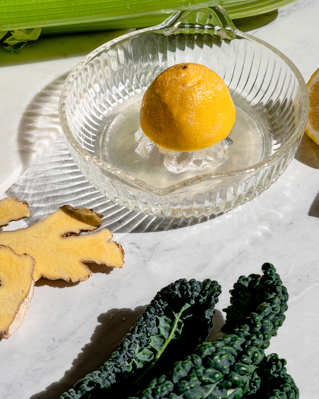 Close up of half a lemon in a glass antique juicer that is next kale, celery, and ginger.