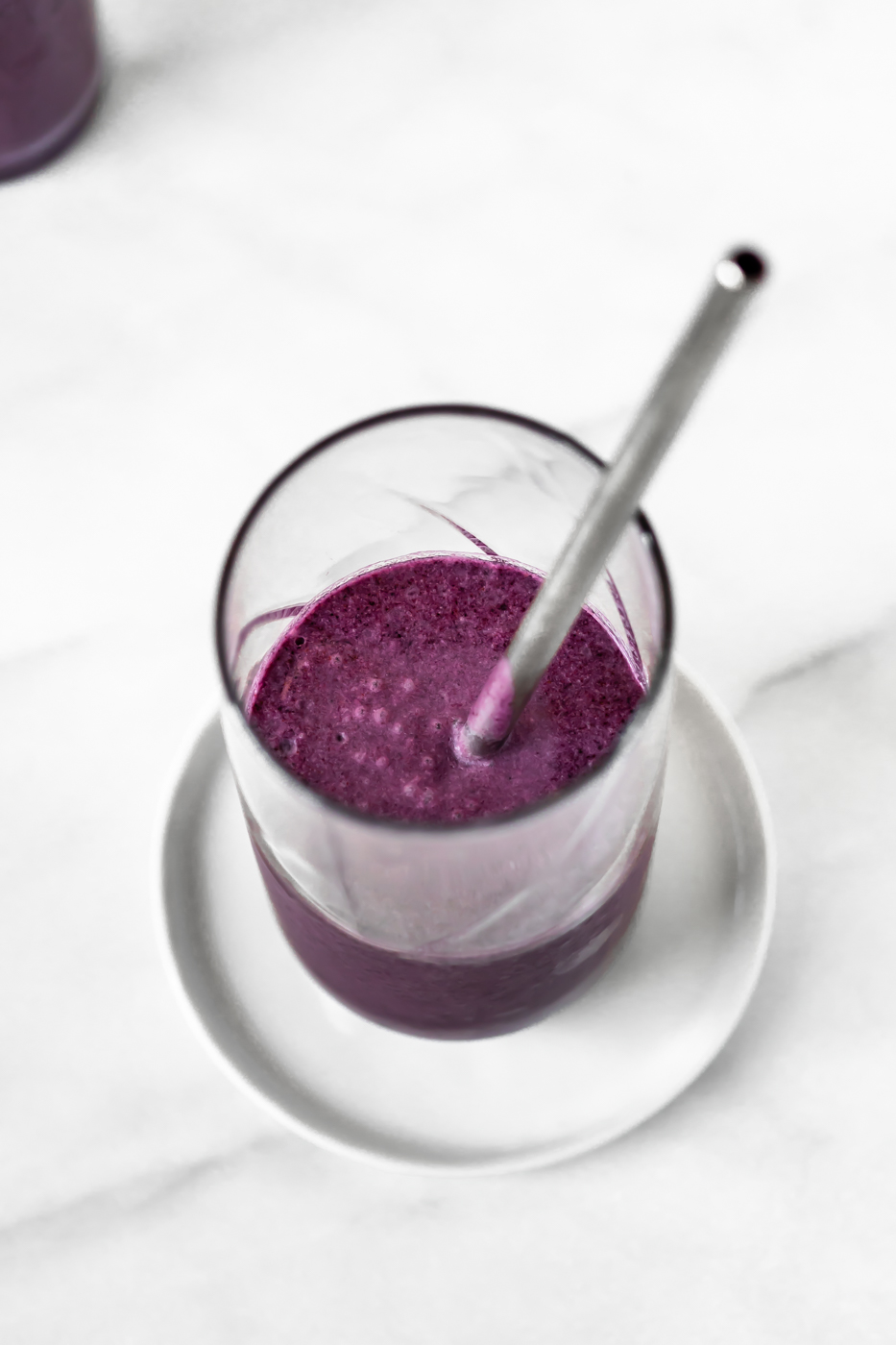 Overhead view of purple smoothie in a glass cup with a metal straw.