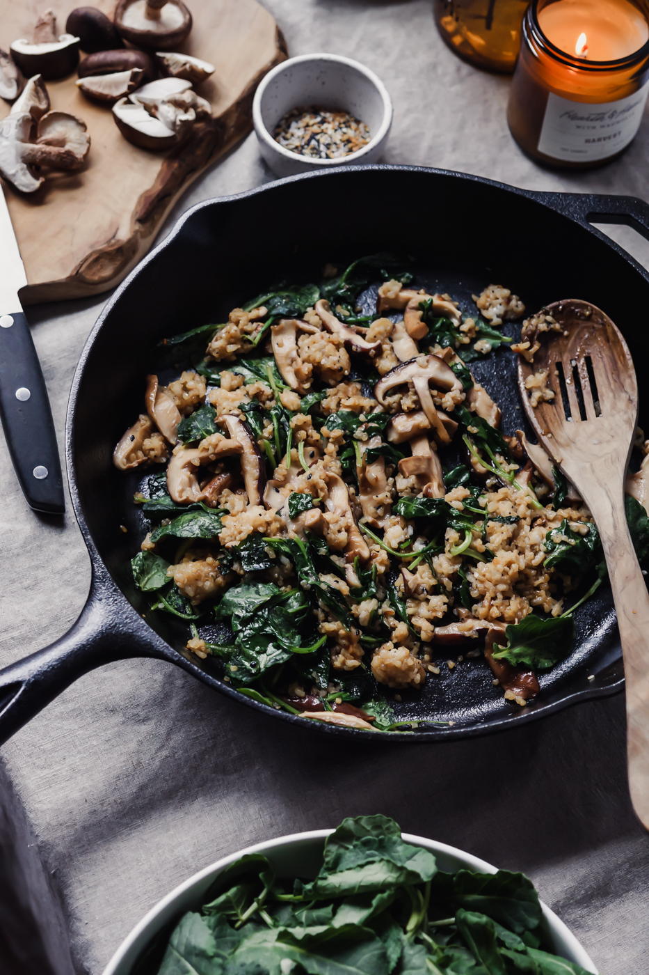 A cast iron skillet that has a mixture of rice, mushrooms, and kale in it.