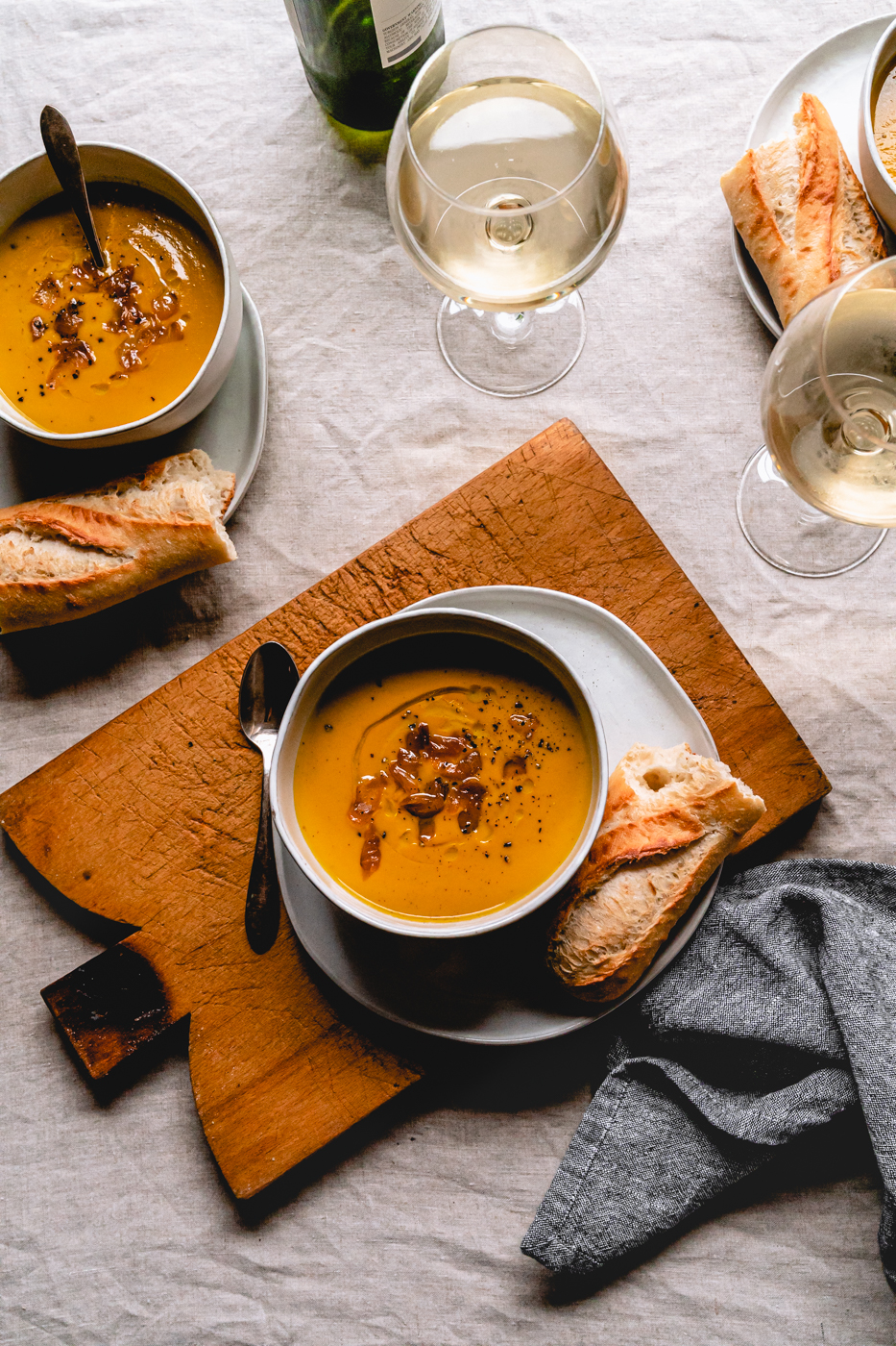 A tablescape photo showing three bowls of instant pot butternut squash soup, wine, and bread ready to be consumed. 