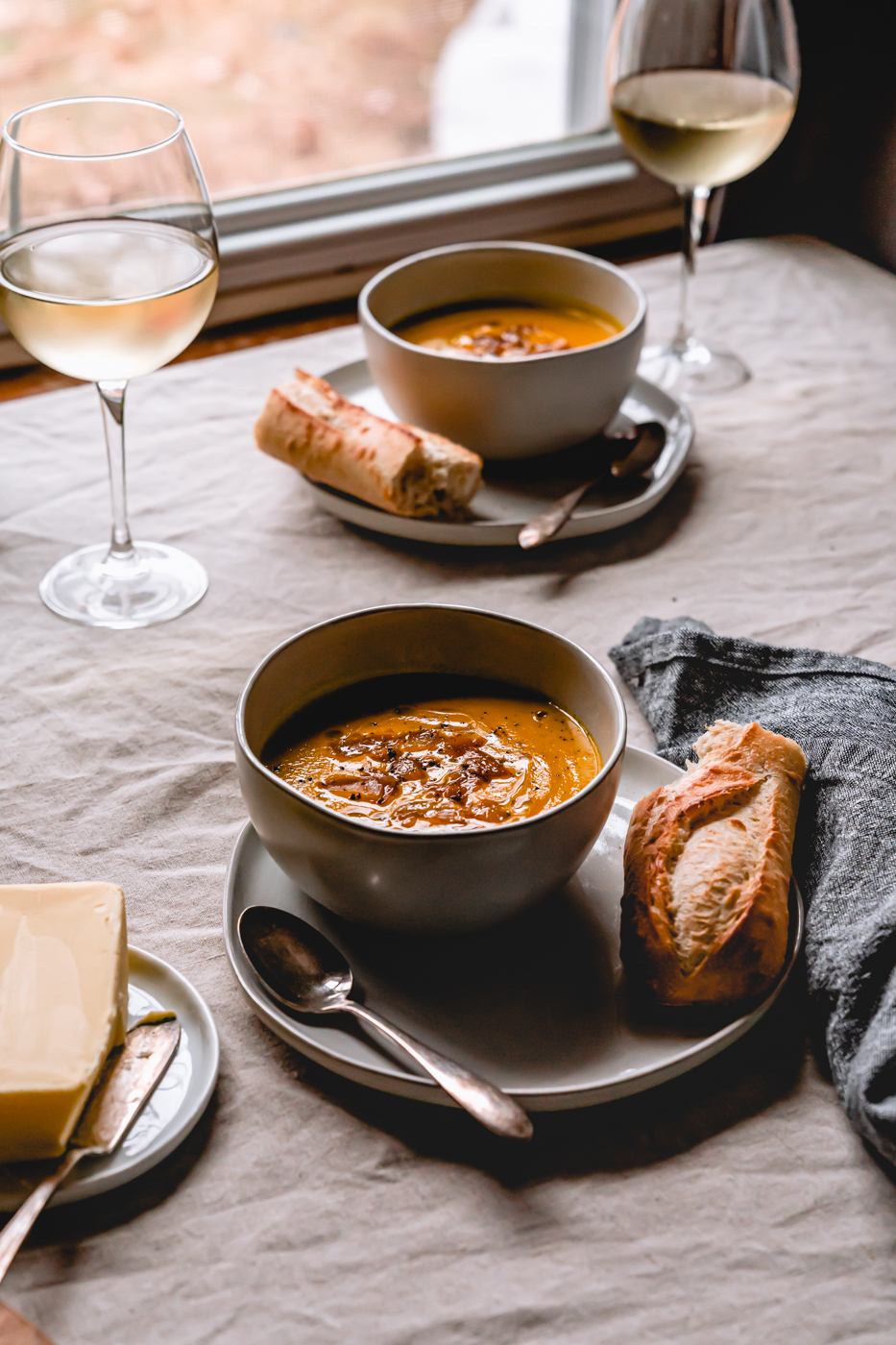 A tablescape photo showing two bowls of instant pot butternut squash soup, wine, bread, and butter ready to be consumed. 