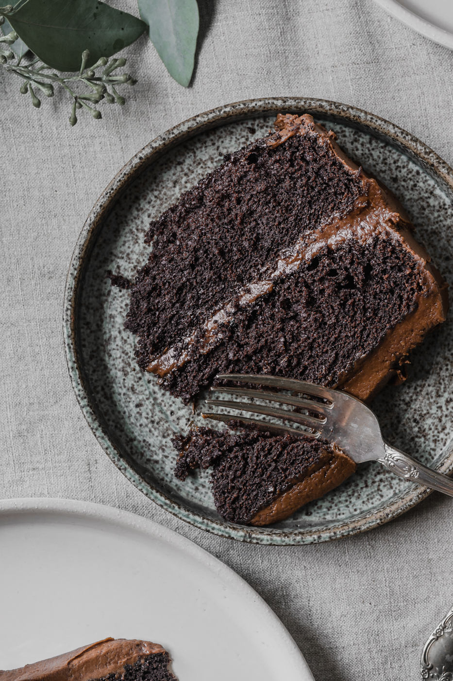 An up close view of a slice of rich gluten-free chocolate cake that is ready to be devoured. You can see the crumb of the cake and the the thick chocolate fudge icing.