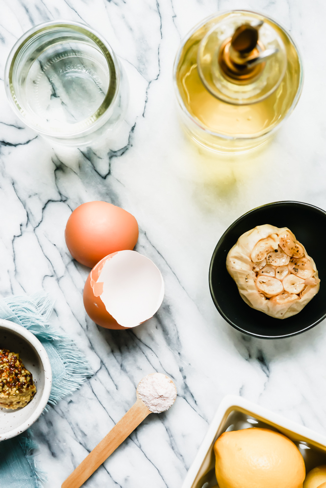 Roasted garlic aioli ingredients set out on a marble counter.