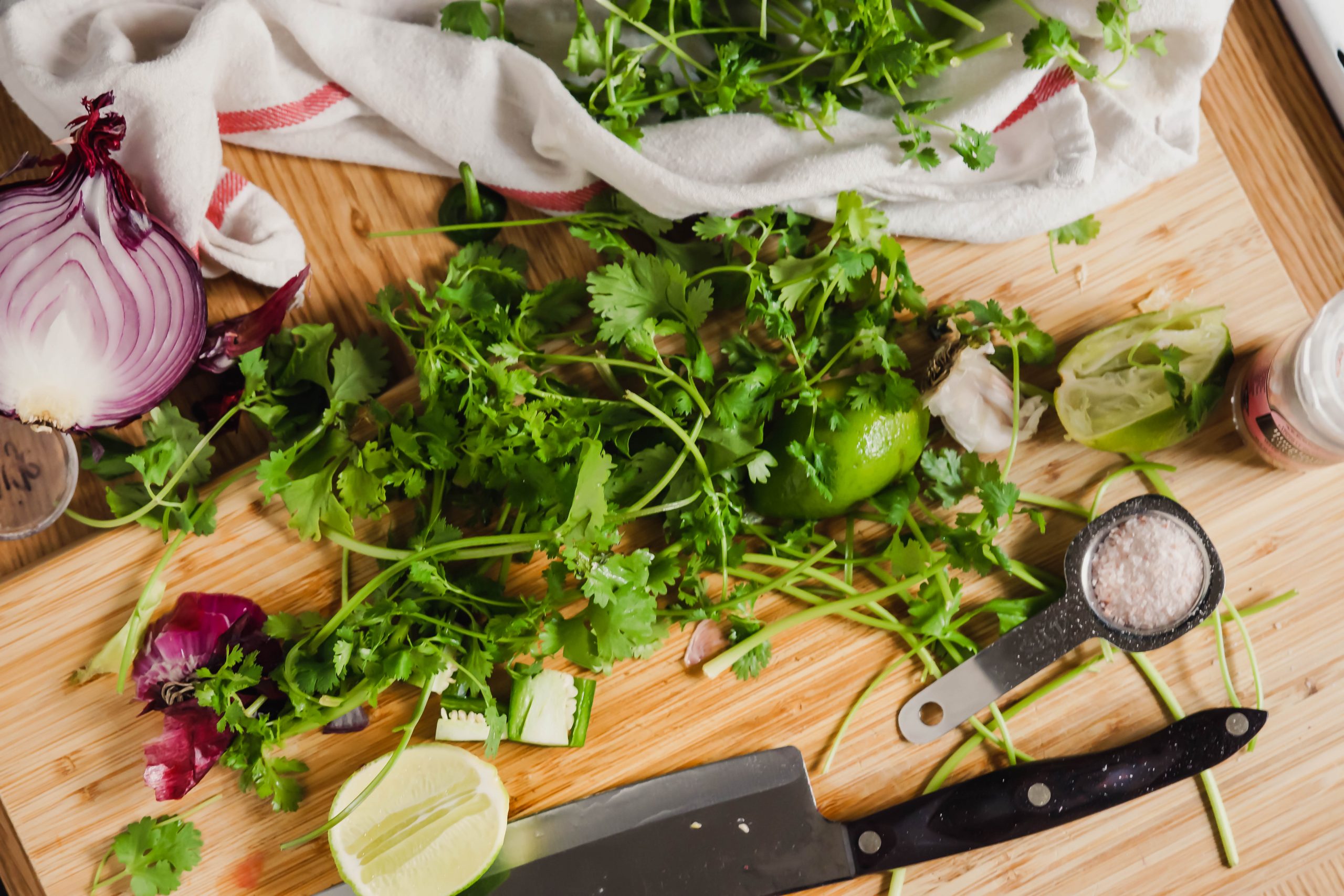 On a wood cutting board, red onion, cilantro, salt, and lime is being prepared for the mango salsa.