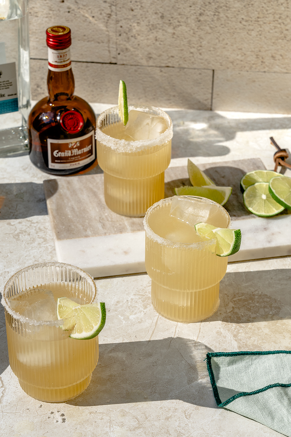 Close up image of a Classic Margarita in a ripple glass with a salt rim and lime wedge garnish. 